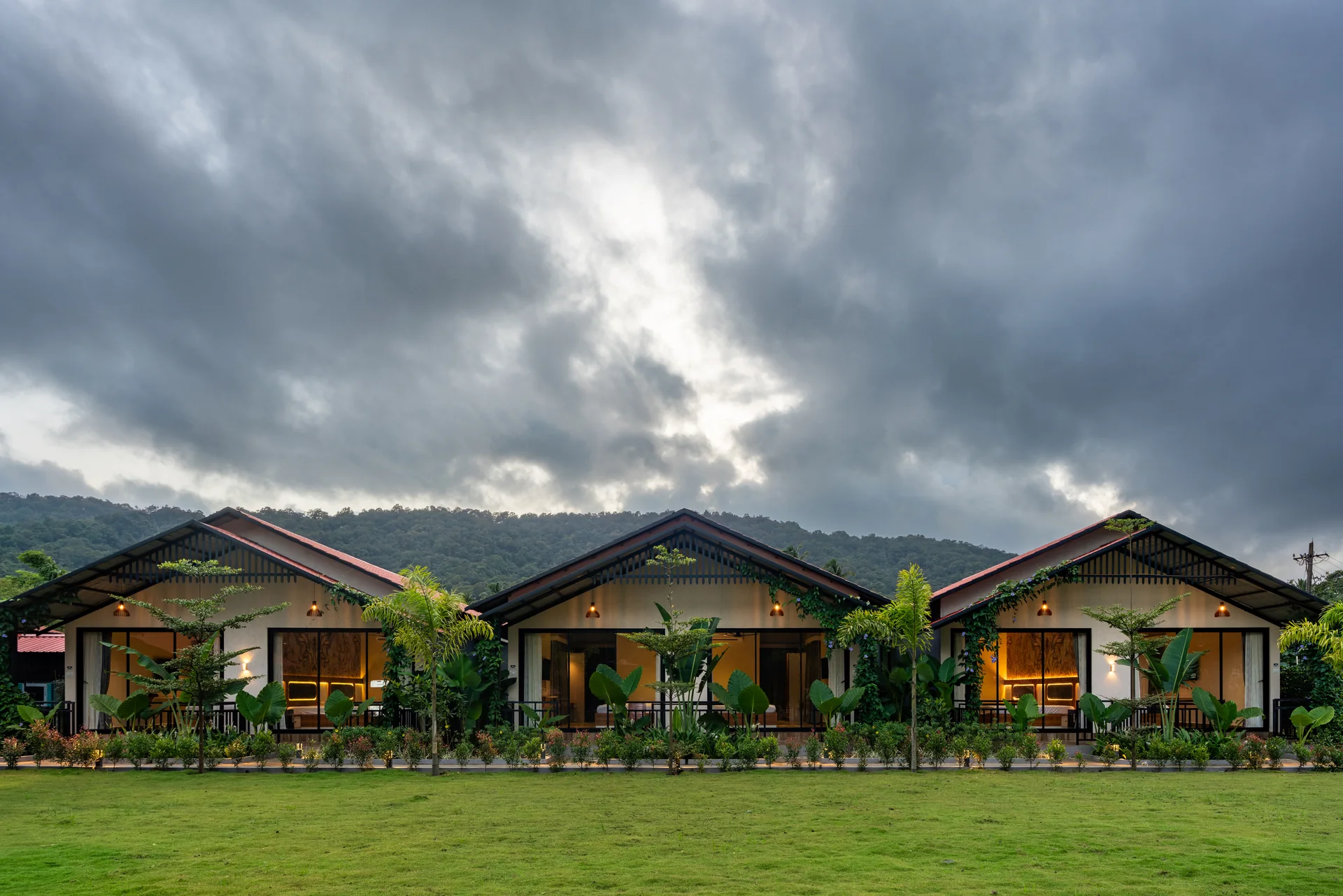 Cottages beneath a dramatic sky at Nadi Teera, Dandeli